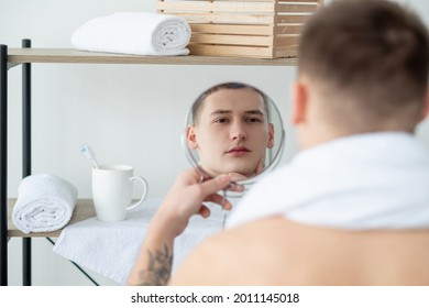 Facial care. Daily routine. Morning grooming. Aftershave lotion. Young handsome man touching smooth clean perfect face admiring mirror reflection in light bathroom.