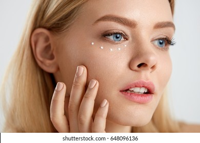 Facial Care. Portrait Of Sexy Young Woman With Drops Of Cosmetic Cream On Skin Under Eyes. Closeup Of Beautiful Female With Beauty Product On Soft Skin, Natural Makeup Touching Face. High Resolution