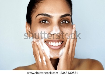 Facial cleansing. Skin care beauty portrait. Young Indian happy woman is applying foam cosmetic product to whole her face to wash it. Daily skincare routine. Dermatology