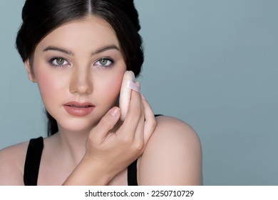 Facial cosmetic makeup concept. Closeup portrait of young charming girl applying dry powder foundation. Beautiful girl smiling with perfect skin putting cosmetic makeup on her face. - Shutterstock ID 2250710729