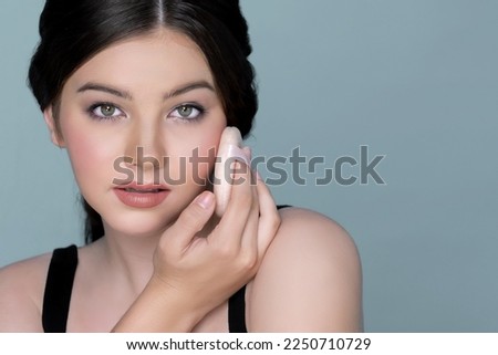 Facial cosmetic makeup concept. Closeup portrait of young charming girl applying dry powder foundation. Beautiful girl smiling with perfect skin putting cosmetic makeup on her face.