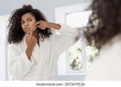 Facial Cosmetology, Skincare Treatment Concept. Young African American Woman Look At Mirror, Squeeze Pimple On Cheek, Worried About Acne Or Skin Problem. Female Stand In Bathroom, Wearing In Bathrobe