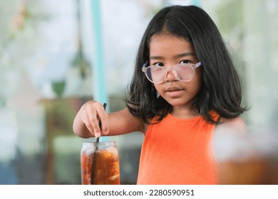 Facial expression of little female kid sitting alone drinking iced lemon tea