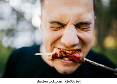 Facial Expression Of Man Eating With Disgust Grilled Sausage Outdoor. Vegetarian Feeling Pain And Suffering Trying Meat. Pork Is Bad. Recycled Dead Animal. Tasteless Fried Food. Adult Male Biting