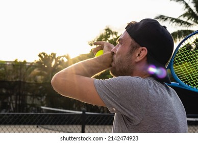 The Facial Expression Of A Man Tennis Player, A Male Athlete Wearing The Cap Holds A Tennis Ball And Racquet And Looks Up. Sportsman Wipes Sweat From His Face.