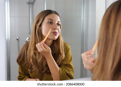 Facial hair removal. Beautiful young woman shaving her face by razor at home. Pretty woman using razor on bathroom.