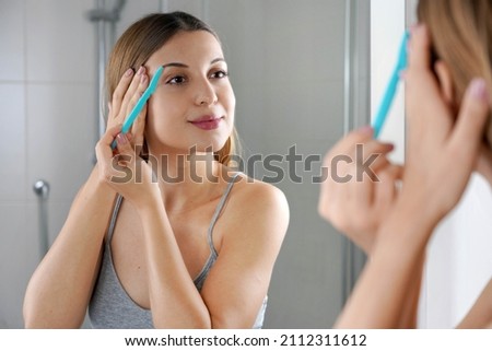 Facial hair removal. Beautiful young woman shaving her face by razor at home. Pretty woman using razor on bathroom.