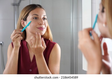 Facial hair removal. Brazilian girl shaving her face by razor at home. Beautiful young woman using razor on bathroom. - Shutterstock ID 2186454589