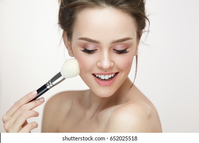Facial Makeup. Closeup Of Beautiful Young Female Model Putting Blush With Cosmetic Brush. Portrait Of Attractive Healthy Girl With Pure Clean Skin And Natural Make-Up. Beauty Concept. High Resolution