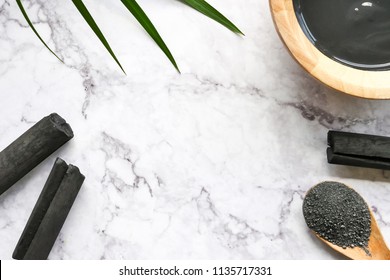 Facial mask and scrub by activated charcoal powder on marble table. Free space for text