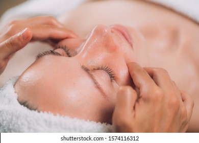 Facial massage beauty treatment. Close-up of a young woman’s face lying on back, getting face lifting massage, pinch and roll technique. 