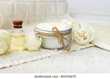 Facial natural cream container, fresh beige garden roses, aroma essential oil, white towel.