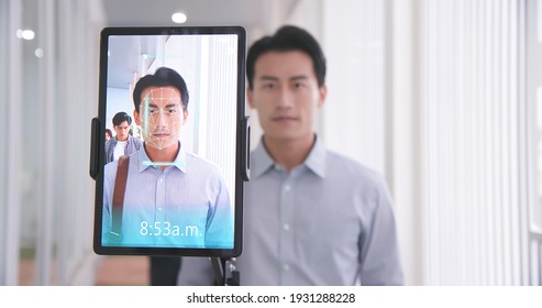 Facial Recognition Concept - Asian Businessman Using Face Scanner To Clock In Work And Check Body Temperature