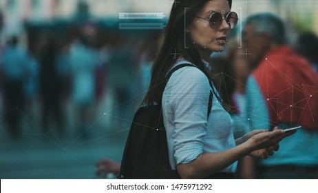 Facial recognition and search and surveillance of a person in the modern digital age, the concept. Young woman with phone in crowd of people on the street, identification and modern technology - Shutterstock ID 1475971292