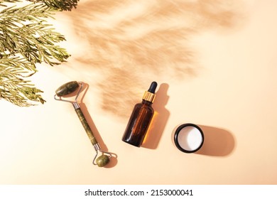 Facial Roller, Serum Bottle And Cream Jar With Cypress Shadow On Light Beige Background. Natural Cosmetics, Aromatherapy, Beauty Treatment Concept. Top View, Flat Lay.