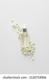 Facial serum in glass dropper bottle with white flowers on light grey background. Cosmetic with hyaluronic acid. Tender spring concept. Natural skin care product for branding. Beauty routine.