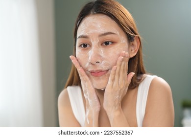 facial skin care routine concept. young woman looking in the mirror during washing her face with facial foam - Powered by Shutterstock