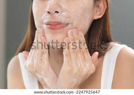 facial skin care routine concept. young woman looking in the mirror during washing her face with facial foam
