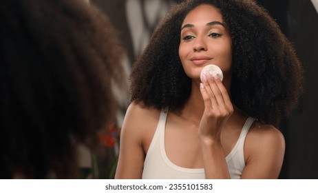 Facial skincare beauty routine African American woman beautiful young girl with cotton pad wipe wash cleaning face remove make up removal skin product looking in mirror reflection dermatology cosmetic - Powered by Shutterstock