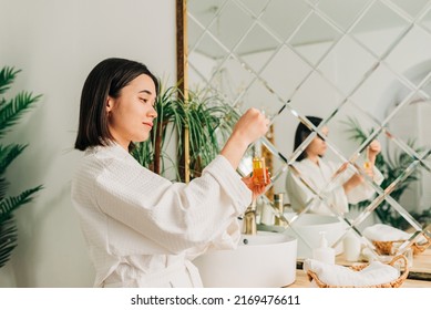 Facial Skincare. Happy Korean Asian Woman Applying Facial Serum Using Dropper Standing In Modern Bathroom.