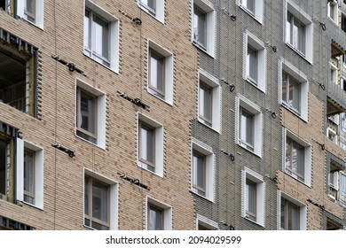 Facing building with ventilated facade. Monolithic concrete frame of apartment building under construction with partially attached ready-made facade cladding blocks.
