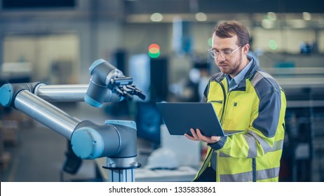At the Factory: Automation Engineer Uses Laptop for Programming Robotic Arm. New Era in Automatic Manufacturing Industry. - Shutterstock ID 1335833861