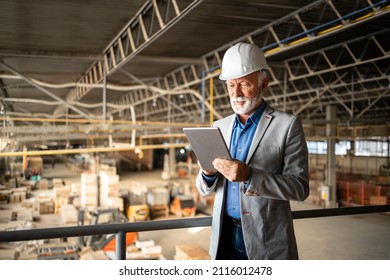 Factory CEO or manager in business suit and hardhat standing in production hall and checking results of his company. Industrial factory interior and forklifts working in background. - Powered by Shutterstock