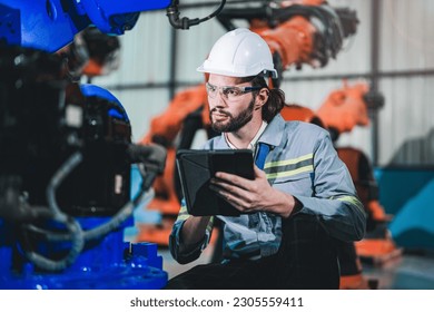 Factory engineer inspecting on machine with smart tablet. Worker works at heavy machine robot arm. The welding machine with a remote system in an industrial factory. Artificial intelligence concept. - Powered by Shutterstock