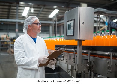 Factory engineer maintaining record on clipboard in drinks production plant