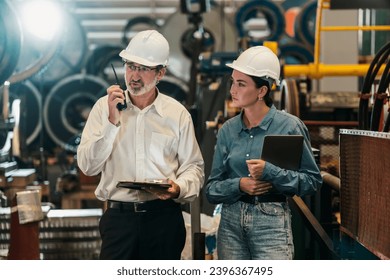 Factory engineer manager with assistant using laptop to conduct inspection of steel industrial machine, exemplifying leadership as machinery engineering inspection supervisor in metalwork manufacture. - Shutterstock ID 2396367495