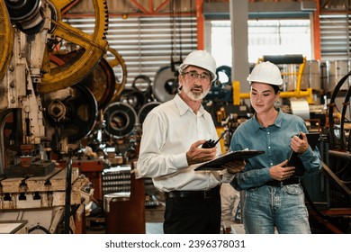 Factory engineer manager with assistant using laptop to conduct inspection of steel industrial machine, exemplifying leadership as machinery engineering inspection supervisor in metalwork manufacture. - Shutterstock ID 2396378031