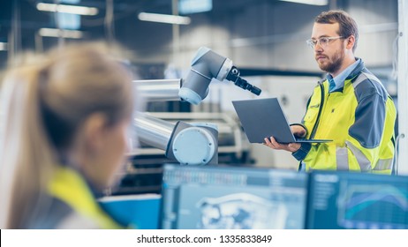 At The Factory: Female Mechanical Engineer Designs 3D Engine On Her Personal Computer, Male Automation Engineer Uses Laptop For Programming Robotic Arm.