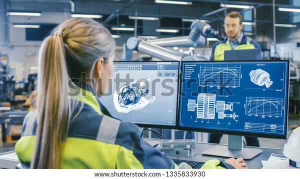 At the Factory:\
Female Mechanical Engineer Designs 3D Engine on Her Personal\
Computer. In the Background Male Automation Engineer who Uses\
Laptop for Programming Robotic\
Arm.