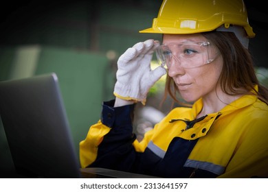 Factory female worker. Engineer  woman worker with laptop working in plant production checking and testing machine in smart factory wearing yellow hard hat safety first at mechanic factory. - Powered by Shutterstock