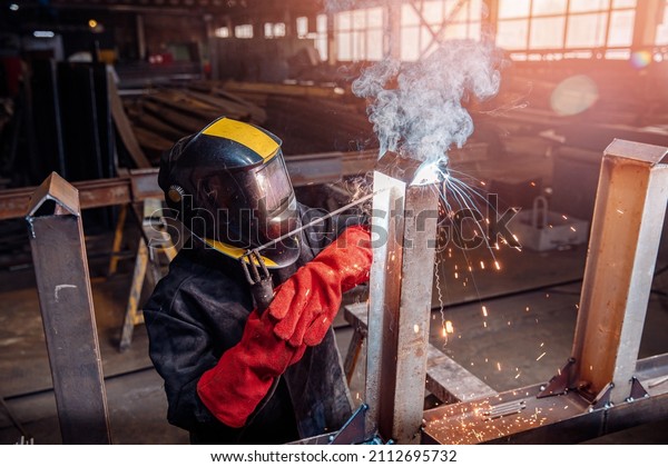 Factory industrial weld worker in\
workplace with spark. Professional welder erecting metal\
steel.