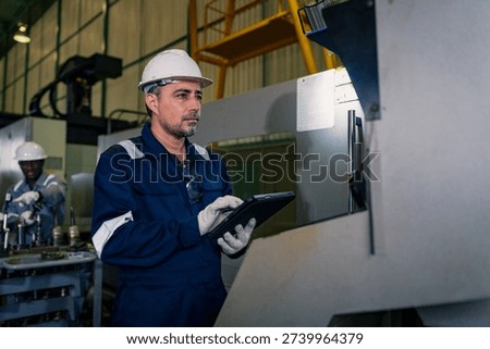 Factory man engineer using digital tablet worker operating CNC machine in manufacturing plant. Professional technician wearing uniform safety helmet maintenance production process heavy equipment
