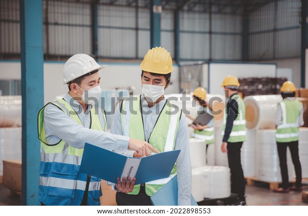 Factory manager and engineer in  medical mask\
and safety protective suite using computer laptop and digital\
tablet working discuss\
together