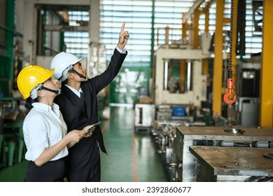 Factory manager point finger to instruct female worker to lift power trolley crane. Man controls crane beam in manufacturing facility. - Powered by Shutterstock