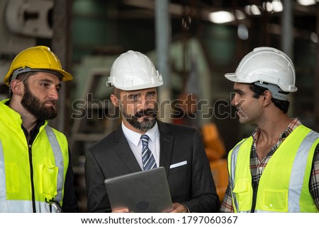 Factory manager in suit using laptop and discussing with industrial engineer ,technician man. They wear helmet or hardhat with safety jackets inside industry manufacturing Facility/Discussion  working