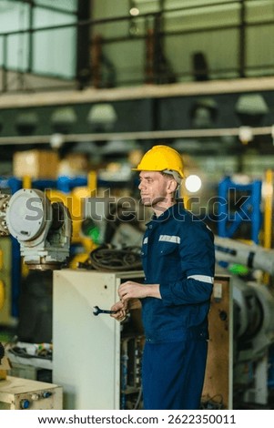 Factory technician performs mechanical maintenance on robotic arm inside industrial facility. Highlighting precision engineering, safety protocols, and automation in modern manufacturing environments