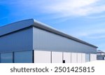 Factory Warehouse Building with Exterior Concrete and Aluminium Steel Wall and Metal Roof against Blue Sky Background, Industry Storage with Automatic Roller Shutter Door and Pavement Floor 