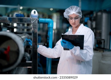 Factory woman worker checking water bottles in the warehouse at the industrial factory. Female worker recording data at the beverages manufacturing line production. - Powered by Shutterstock