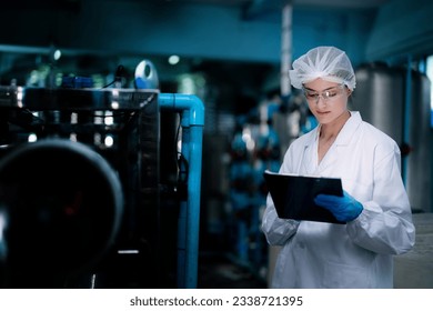 Factory woman worker checking water bottles in the warehouse at the industrial factory. Female worker recording data at the beverages manufacturing line production. - Powered by Shutterstock