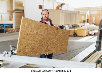 Factory worker or carpenter carrying a sheet of chipboard in an industrial warehouse for use during the production and manufacturing process - Shutterstock ID 2058887171