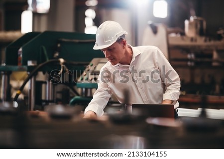 Factory worker checking electrical machine process at industrial worksite , wearing hard hat for safety