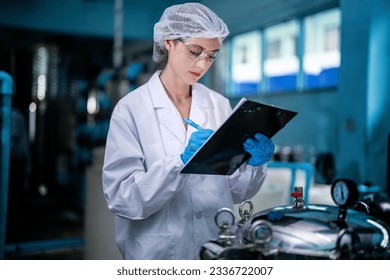 Factory worker checking water bottles in the warehouse at the industrial factory. Female worker recording data at the beverages manufacturing line production. - Powered by Shutterstock - Get 15% off with code: PIKWIZARD15