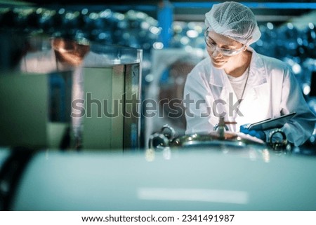 Factory worker checking water bottles in the warehouse at the industrial factory. Female worker recording data at the beverages manufacturing line production.