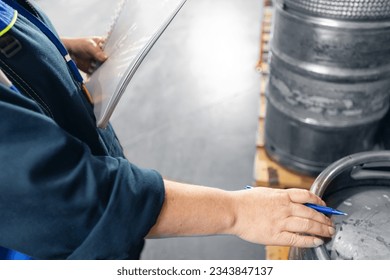 Factory worker with computer tablet inspecting kegs with beer in warehouse of modern brewery stock, blurred background. - Powered by Shutterstock