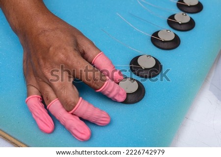 A factory worker double checking a set of piezoelectric diaphragms placed on a foam sheet. Example of quality control.