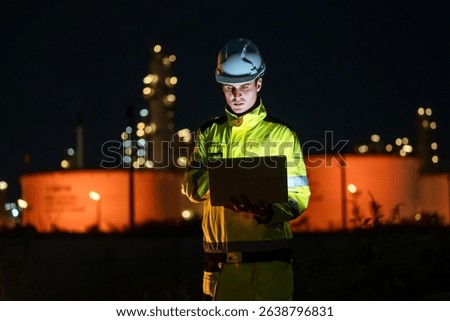 Factory worker engineer man using laptop computer for system maintenance at outdoor refinery site during night shift, working in industrial environment with focus and precision.